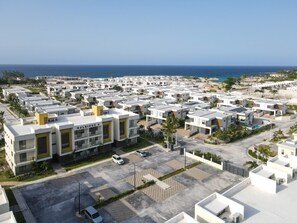 Un complexe résidentiel moderne composé de plusieurs bâtiments blancs, doté d’un espace de stationnement et offrant une vue sur l’océan.