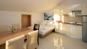 Una camera moderna e compatta con un letto, un tavolo da pranzo con sedie, un angolo cottura e un quadro appeso al muro.