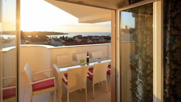 Un balcone con tavolo e sedie, una bottiglia di vino e vista sul mare e sugli edifici.