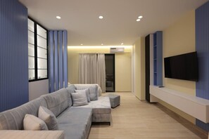 Un salon moderne avec un canapé d’angle, un téléviseur à écran plat fixé au mur et un meuble de rangement intégré pour les appareils multimédias.