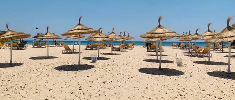 Une plage avec des parasols en chaume et des chaises longues.