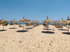 Uma praia com guarda-sóis de palha e espreguiçadeiras.