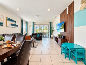 A modern living room with a dining area, a sofa, a TV mounted on the wall, and a view through the glass door. - Family Villa in Windsor • Lazy River • BBQ • Pool (Kissimmee)