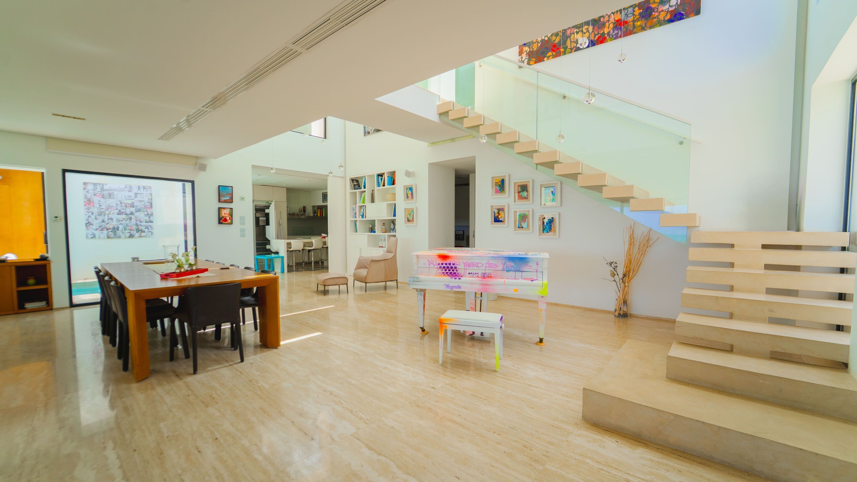 Un intérieur spacieux et moderne, avec une table à manger en bois, des chaises, un escalier et un mur décoratif où sont exposées des œuvres d'art.