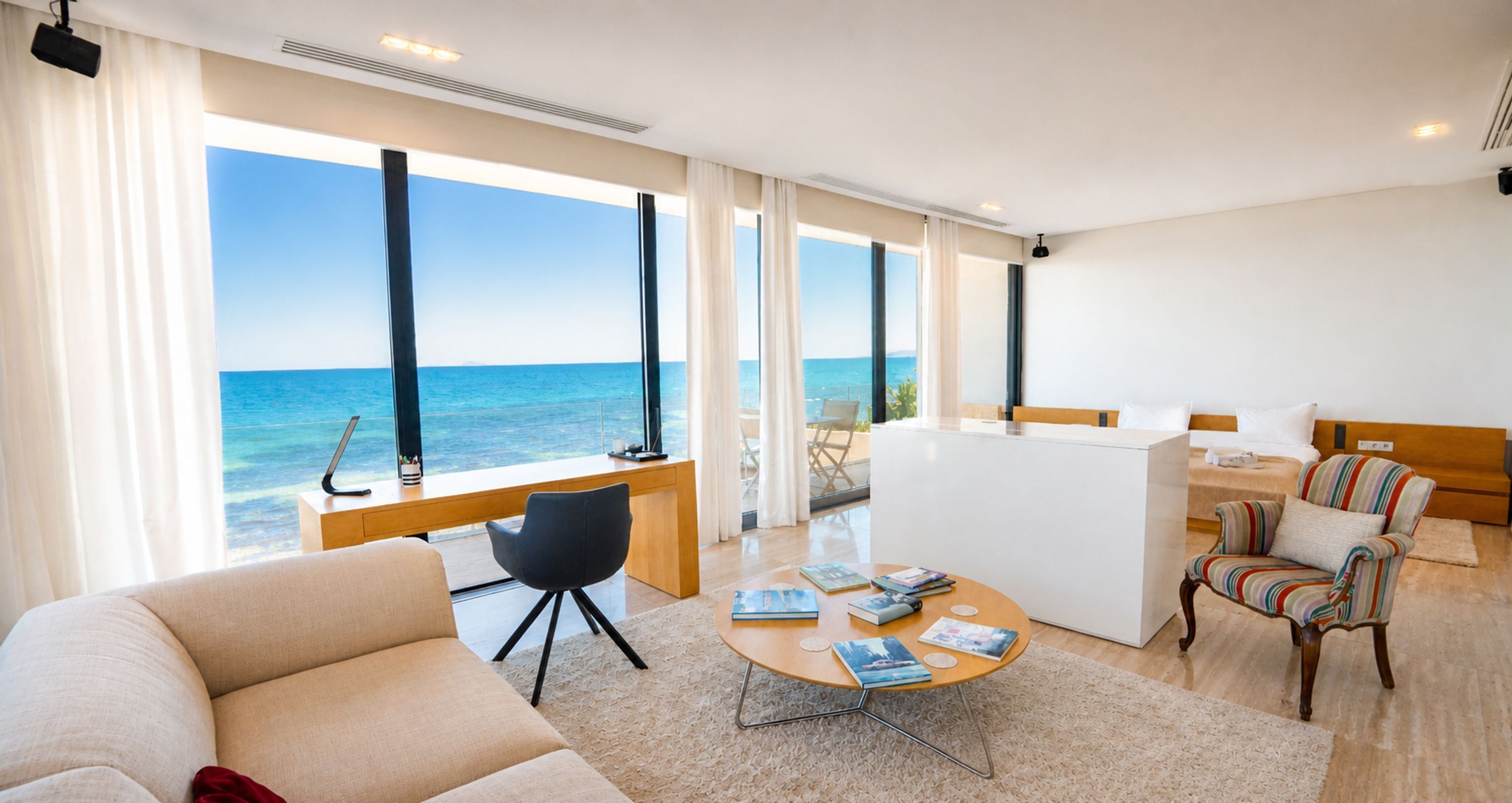Une chambre d’hôtel moderne dotée d’une grande fenêtre donnant sur la mer, d’un coin salon confortable et d’une petite kitchenette.
