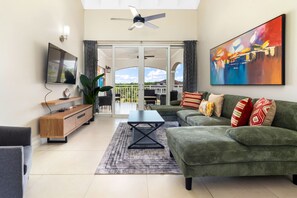 A modern living room with a green sofa, a coffee table, and a flat-screen TV. - 3rd Floor Condo Richmond Estate ~Beach Access~Pool (Plantation Village)