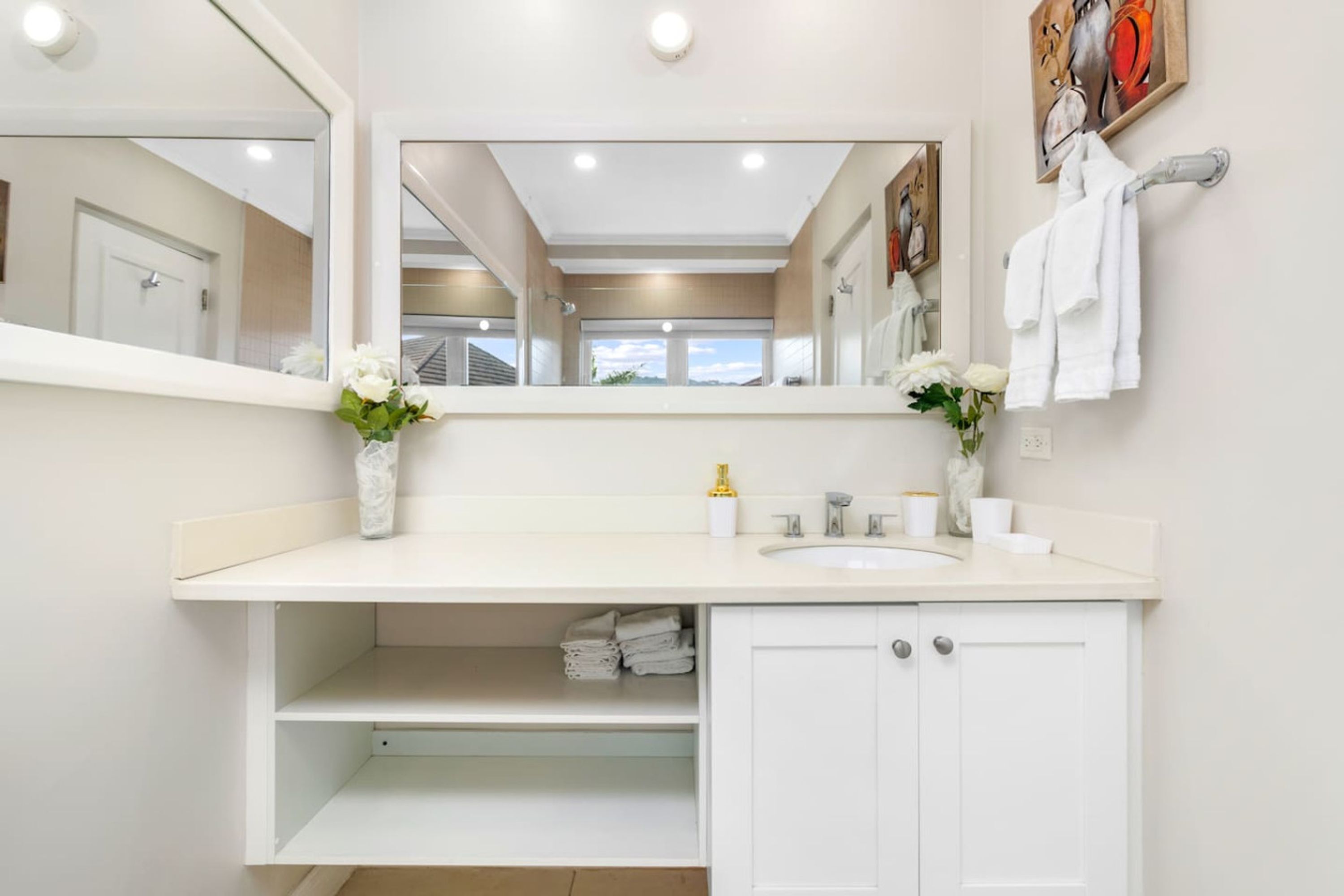 Un baño moderno con tocador blanco, un espejo grande y vistas al exterior.