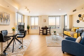A modern living room with a sofa, a dining table, and a TV. - Downtown Silver Spring Walkable Metro Skyline Balcony Corner Suite | Luxe Pad (Silver Spring)