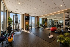 Ett gym med träningsutrustning, en svart matta och utsikt över staden.