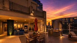 A rooftop terrace with a dining area, outdoor seating, a grill, and a city skyline view at sunset. - Midtown Atlanta 1BR Skyline Balcony Corner Condo by Piedmont Park | Luxe Pad (Atlanta)