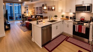 A modern kitchen with white cabinets, stainless steel appliances, and a large window overlooking a cityscape. - Midtown Atlanta 1BR Skyline Balcony Corner Condo by Piedmont Park | Luxe Pad (Atlanta)