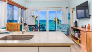 A kitchen with a view of the ocean, a dining area with chairs, and a TV mounted on the wall. - Teal Horizon~OceanfrontCaribbean Escape~Tower Isle (Tower Isle)