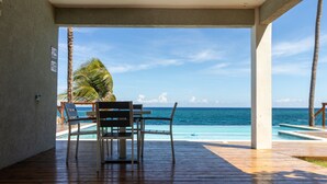 A wooden deck with a table and chairs overlooking a pool and the ocean. - Teal Horizon~OceanfrontCaribbean Escape~Tower Isle (Tower Isle)