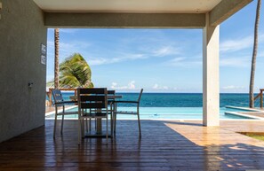 A wooden deck with a table and chairs overlooking a pool and the ocean. - Teal Horizon~OceanfrontCaribbean Escape~Tower Isle (Tower Isle)