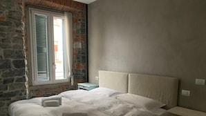 A bedroom with a stone wall, a bed with white linens, a nightstand, and a window with shutters. - Romantic Chic Apartment (Como)