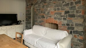 A room with a stone fireplace, a white sofa, a wooden table, and a television on a cabinet. - Romantic Chic Apartment (Como)