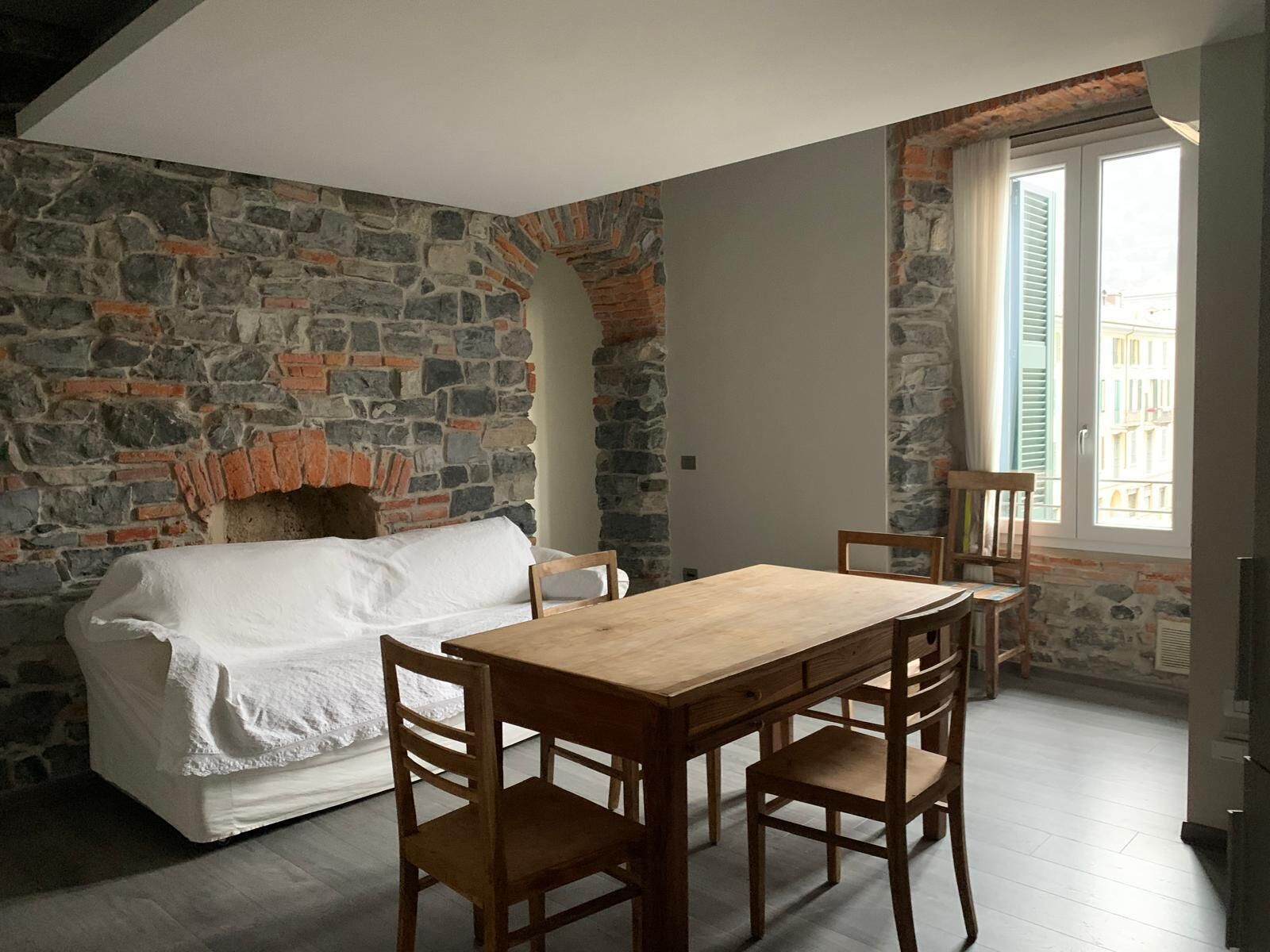 A cozy room with a stone wall, a fireplace, a wooden dining table with chairs, and a white sofa.