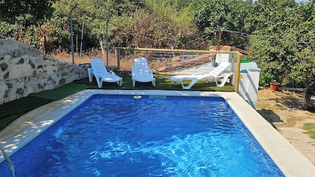 A swimming pool with white lounge chairs and a stone wall. - Rural House Parajes del Chanza (Cortegana)