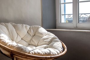 Une chaise en osier dotée d’un siège et d’un dossier rembourrés, placée près d’une fenêtre donnant sur un balcon.