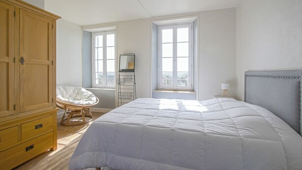 Ein Schlafzimmer mit einem großen Bett, einem Holzschrank, einem Korbstuhl und einem Fenster mit Blick.