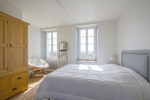 Una camera da letto con un letto grande, un'armadio in legno, una sedia in vimini e una finestra con vista.