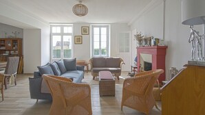 Ein geräumiges Wohnzimmer mit grauem Sofa, braunem Sofa, Korbstühlen, Kamin und Essbereich mit Holzschrank und Stühlen.