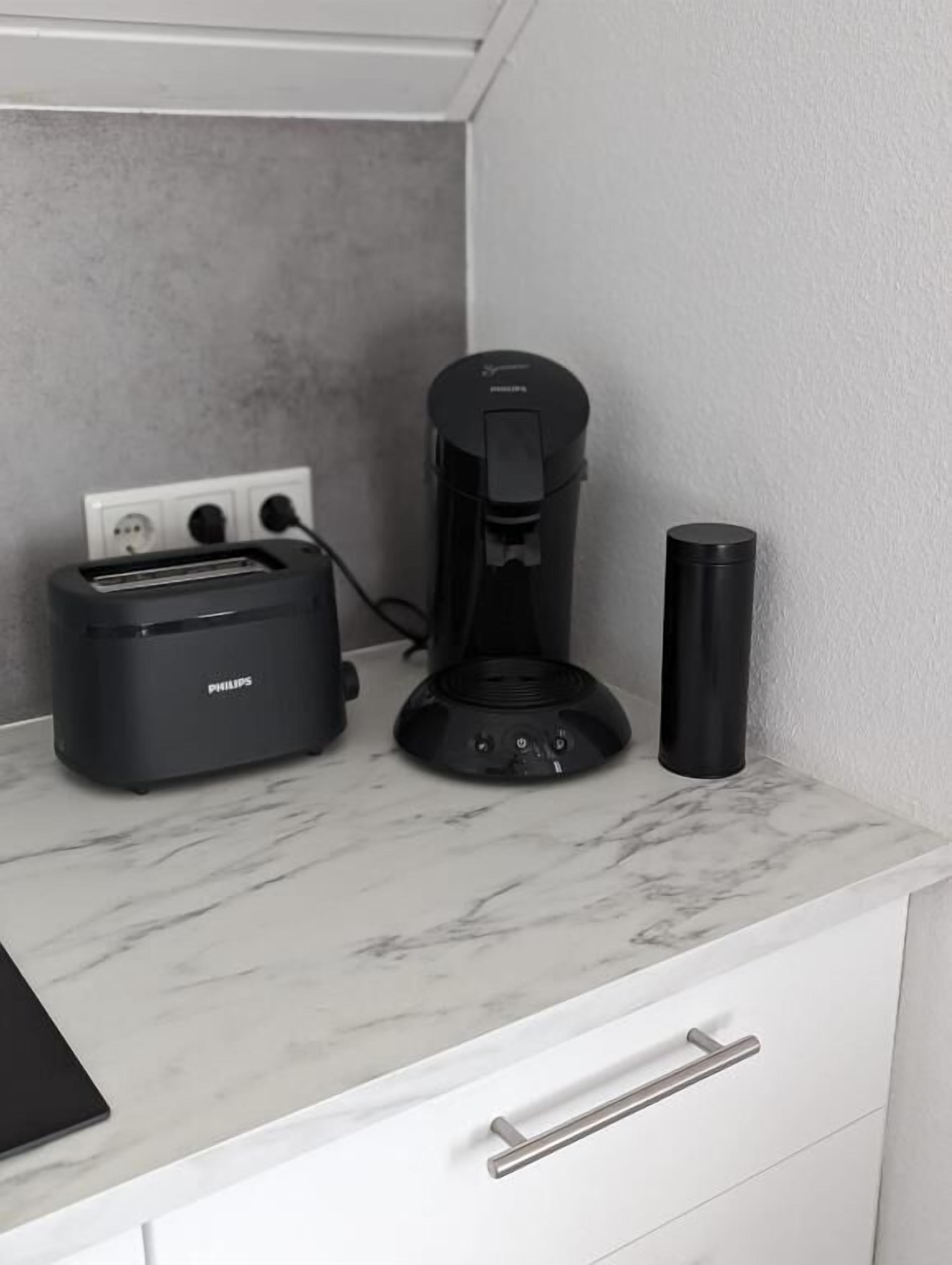Uma bancada de cozinha com uma torradeira Philips, uma cafeteira e um copo preto.