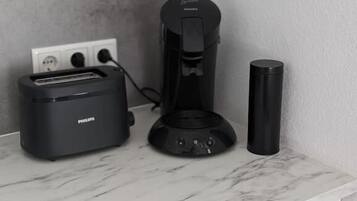 Uma bancada de cozinha com uma torradeira Philips, uma cafeteira e um copo preto.