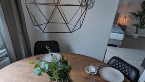 Ett runt matbord med en träskiva, omgivet av stolar. Ett dekorativt mittstycke med grönt och en geometrisk lampa ovanför bordet syns.