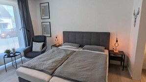 Ett modernt sovrum med en stor säng, en stol, sängbord och ett fönster med gardiner.