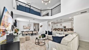 A spacious living area with a high ceiling, a staircase, and a kitchen in the background. - Fabulous Villa 5Bd Pool   Spa - Next to Disney 611 (Davenport)