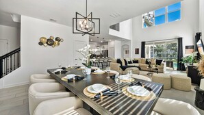 A spacious living area with a high ceiling, a dining table set for six, and a large window offering a view of the outdoors. - Fabulous Villa 5Bd Pool   Spa - Next to Disney 611 (Davenport)