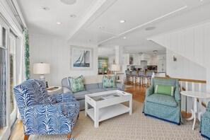 A spacious living room with a sofa, armchair, and coffee table. A kitchen and dining area are visible in the background. - Coastal Luxe at Harris Lane (Kennebunk)