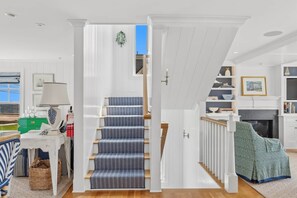 A staircase with a patterned carpet, white walls, and a view of the outside. - Coastal Luxe at Harris Lane (Kennebunk)