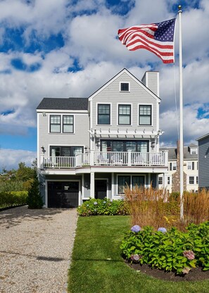 A two-story house with a balcony, a garage, and a well-maintained lawn. - Coastal Luxe at Harris Lane (Kennebunk)