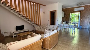 A living room with a staircase, wicker furniture, a TV, and a dining area with a table and chairs. - Vacation home Sorrento Peninsula (Vico Equense)