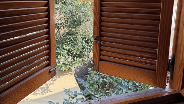 A wooden door with horizontal slats, leading to an outdoor area with a tiled floor and a small plant. - Vacation home Sorrento Peninsula (Vico Equense)