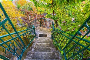 A staircase with green railings surrounded by lush greenery and trees. - Apartment with Garden (Durrës)