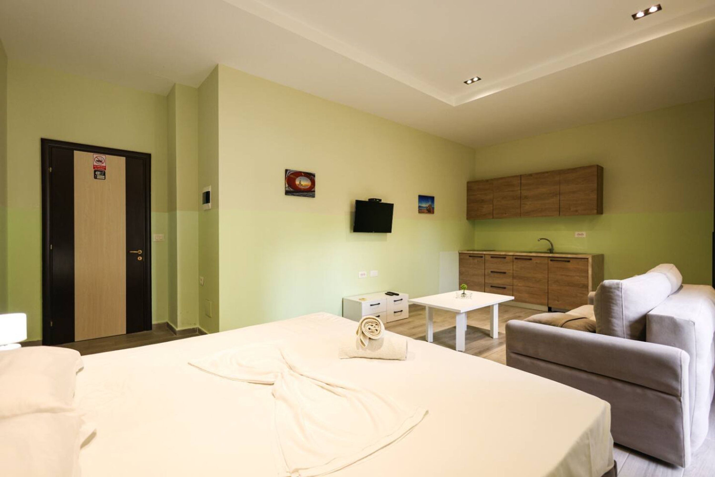 A hotel room with a bed, a small table, a sofa, a cabinet, and a television.