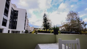 A balcony with a white table and chair, overlooking a cityscape with modern buildings and a tree with yellow flowers. - Azzurra Studio 03 in Durrës (Durrës)