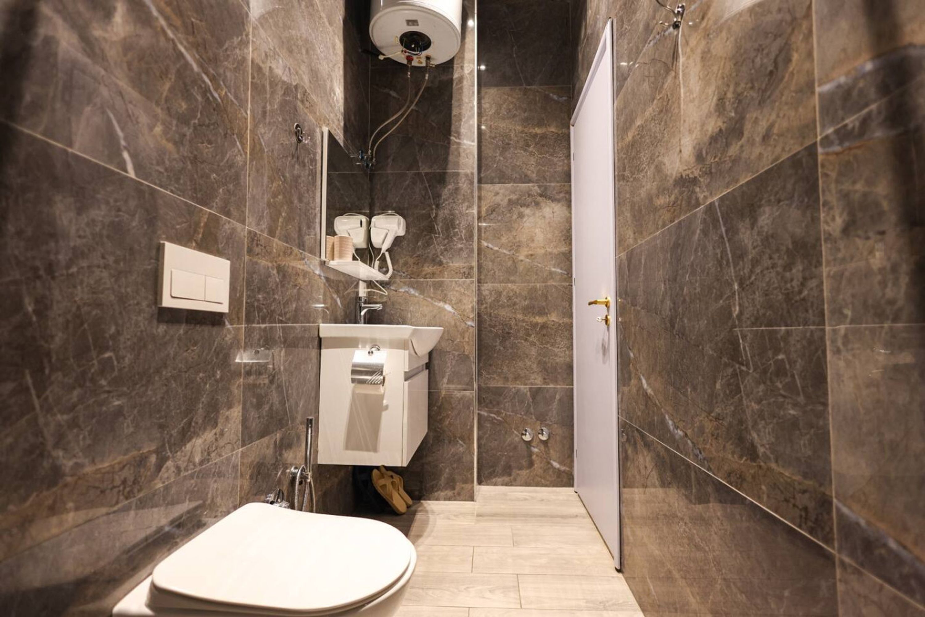 A modern bathroom with a marble wall, a toilet, a sink, and a shower area.