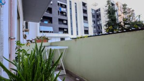Een balkon met een bloempot, een tafeltje en uitzicht op meerhoogbouw.