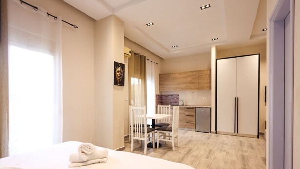 Een hotelkamer met een bed, een klein tafeltje en stoelen. Er is een kitchenette met kastjes en een koelkast.