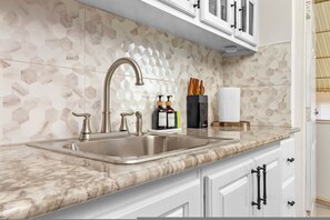 A kitchen with a marble countertop, a stainless steel sink, and white cabinets with black handles. - 3rd Floor Condo~ Tower Isle~24hr Security (Tower Isle)