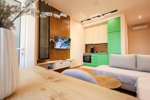 Een moderne woonkamer met een houten vloer, een grijze bank, een klein rond salontafeltje en een tv die aan een houten wand is bevestigd.