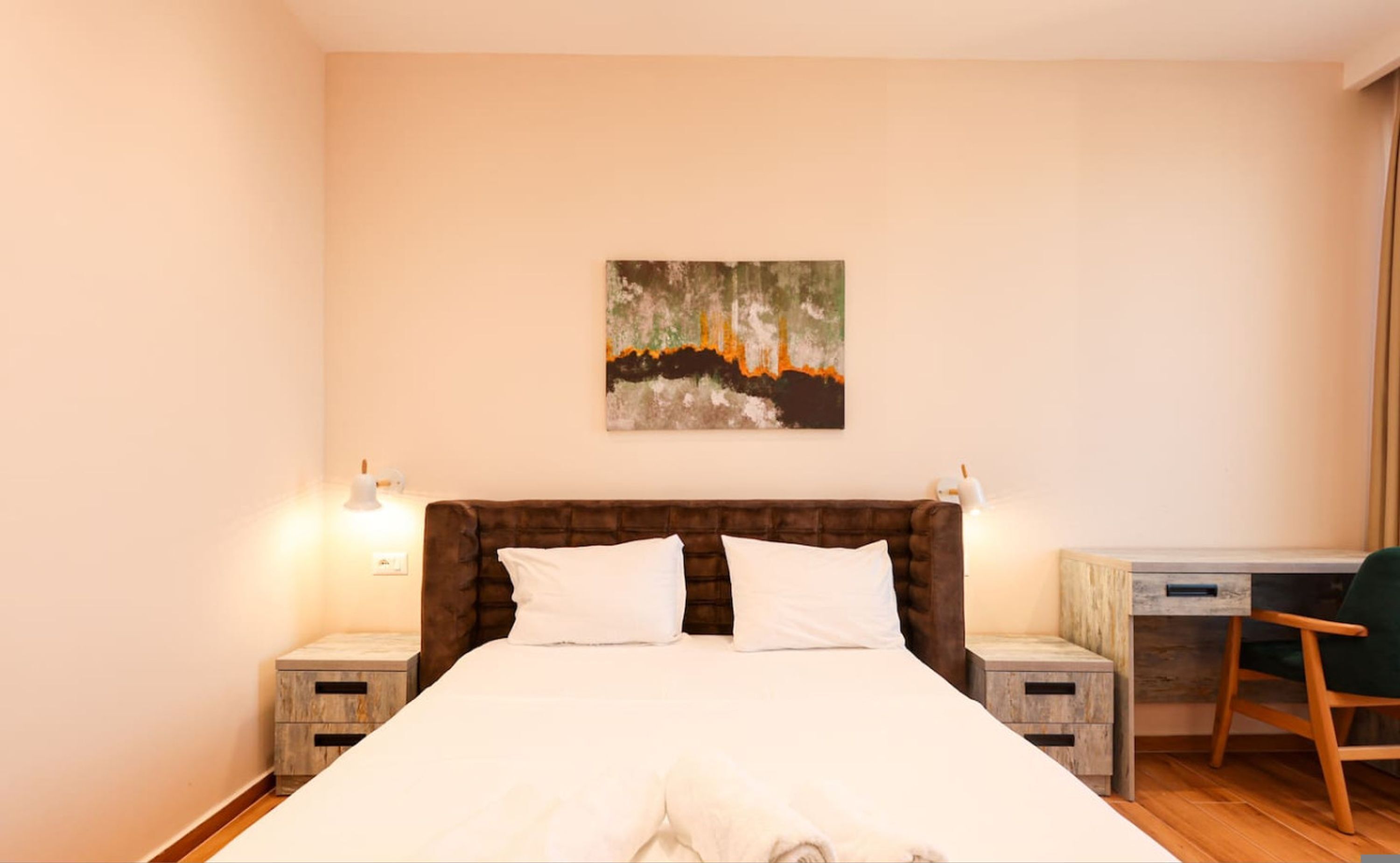 Een slaapkamer met een groot bed, twee nachtkastjes, een bureau, een stoel en een schilderij aan de muur.