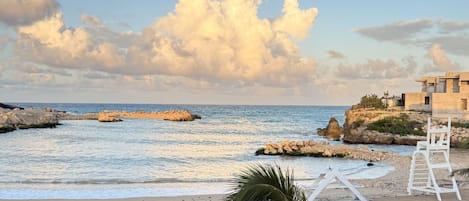 A beach with a clear sky, rocky outcrops, and a white structure with a ladder.