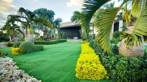 A well-manicured garden with palm trees, a neatly trimmed lawn, and a building labeled "RADISIAC BEACH CLUB". - Sun-Soaked Paradisiac Escape|3BR, Private Beach, Pool (Plantation Village)