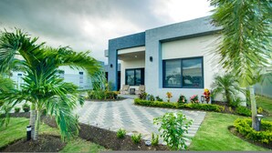 A modern two-story house with a paved patio, surrounded by lush greenery and palm trees. - Sun-Soaked Paradisiac Escape|3BR, Private Beach, Pool (Plantation Village)
