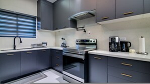 A modern kitchen with dark cabinets, stainless steel appliances, and a window with blinds. - Sun-Soaked Paradisiac Escape|3BR, Private Beach, Pool (Plantation Village)